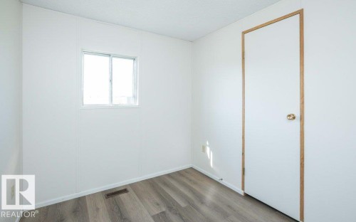 White paneled walls with wood-finish flooring, featuring a window and a door with a brass knob - 26417 Twp Rd 582, Rural Westlock County, AB - Indoor Photo Showing Other Room