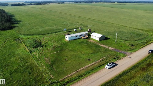 Expansive green fields surrounding the property, a single-story residence, a detached auxiliary building, and a dirt road frontage - 26417 Twp Rd 582, Rural Westlock County, AB - Outdoor With View