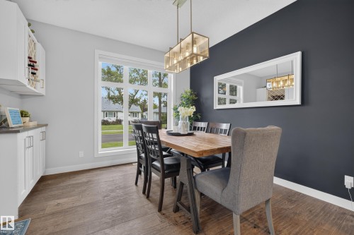 Wood-finish flooring, built-in cabinetry with wine storage, large multi-pane window, and a linear chandelier - 11018 122 Street Nw, Edmonton, AB - Indoor Photo Showing Dining Room