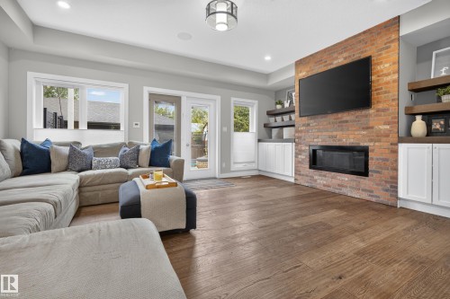 Wood-finish flooring, brick-faced wall with built-in fireplace, built-in cabinetry with wood shelves, recessed lighting, and patio doors - 11018 122 Street Nw, Edmonton, AB - Indoor Photo Showing Living Room With Fireplace