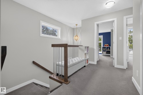 Carpeted upper landing with a contemporary open railing, built-in bench, and a modern chandelier - 11018 122 Street Nw, Edmonton, AB - Indoor