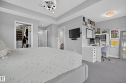 Tray ceiling with recessed lighting, built-in closet organization system, carpeted flooring, wall-mounted television, and a built-in desk unit - 