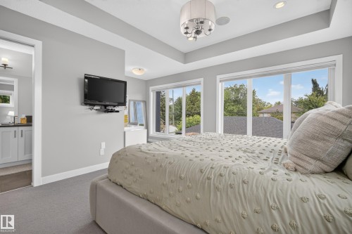 Recessed tray ceiling with a contemporary chandelier, multiple windows with roller shades, and plush carpeting - 11018 122 Street Nw, Edmonton, AB - Indoor Photo Showing Bedroom