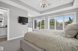 Recessed tray ceiling with a contemporary chandelier, multiple windows with roller shades, and plush carpeting - 