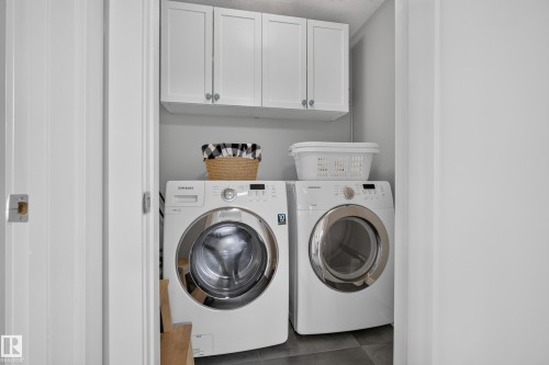 Dedicated laundry area featuring white upper cabinetry, a light gray wall finish, and dark gray floor tiling - 11018 122 Street Nw, Edmonton, AB - Indoor Photo Showing Laundry Room
