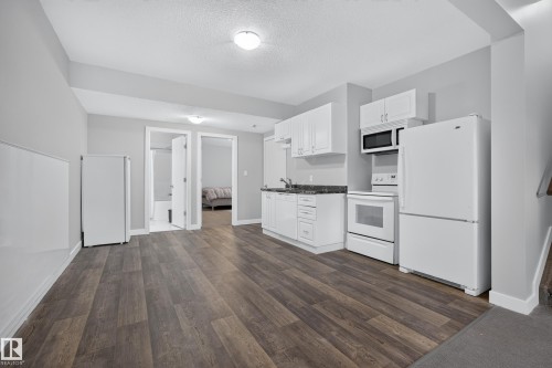 Compact kitchen featuring white cabinetry, dark countertops, and white appliances including a refrigerator, range, and microwave - 11018 122 Street Nw, Edmonton, AB - Indoor Photo Showing Kitchen