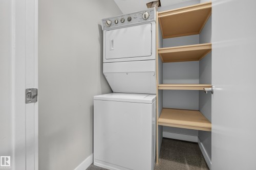 Stackable washer and dryer with adjacent built-in shelving - 11018 122 Street Nw, Edmonton, AB - Indoor Photo Showing Laundry Room