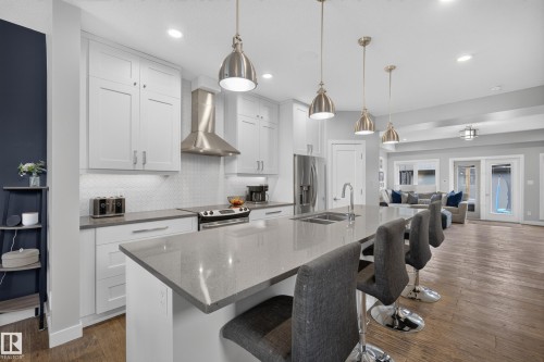 Modern kitchen featuring white cabinetry, stainless steel appliances, a large center island with integrated sink, pendant lighting, and wood-finish flooring - 11018 122 Street Nw, Edmonton, AB - Indoor Photo Showing Kitchen With Double Sink With Upgraded Kitchen