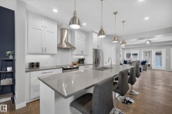 Modern kitchen featuring white cabinetry, stainless steel appliances, a large center island with integrated sink, pendant lighting, and wood-finish flooring - 