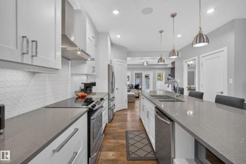 Kitchen featuring white shaker cabinetry, stainless steel appliances, a tile backsplash, wood-finish flooring, and a large center island with pendant lighting - 11018 122 Street Nw, Edmonton, AB - Indoor Photo Showing Kitchen With Double Sink With Upgraded Kitchen