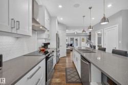 Kitchen featuring white shaker cabinetry, stainless steel appliances, a tile backsplash, wood-finish flooring, and a large center island with pendant lighting - 