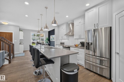 Kitchen featuring a large island with an undermount sink, pendant lighting, stainless steel appliances, white cabinetry, and wood-finish flooring - 11018 122 Street Nw, Edmonton, AB - Indoor Photo Showing Kitchen With Stainless Steel Kitchen With Upgraded Kitchen