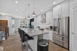 Kitchen featuring a large island with an undermount sink, pendant lighting, stainless steel appliances, white cabinetry, and wood-finish flooring - 