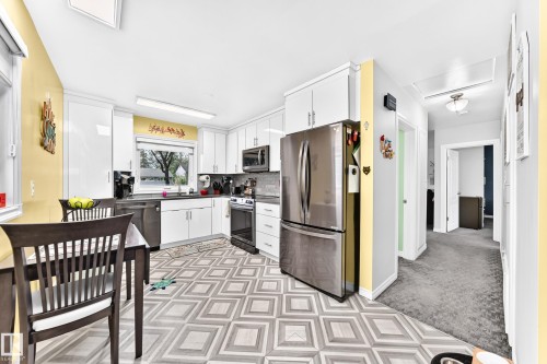Kitchen featuring white cabinetry, stainless steel appliances, patterned flooring, and a large window - 10524 128 Avenue Nw, Edmonton, AB - Indoor Photo Showing Other Room