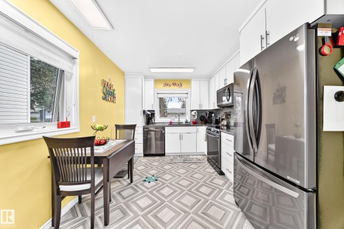 Kitchen featuring white cabinetry, stainless steel appliances, dark countertops, and patterned floor tile - 10524 128 Avenue Nw, Edmonton, AB - Indoor Photo Showing Kitchen