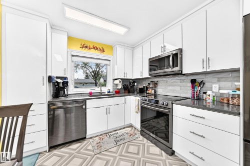 White cabinetry with brushed nickel hardware, stainless steel appliances, dark countertops, a tiled backsplash, and geometric pattern flooring - 10524 128 Avenue Nw, Edmonton, AB - Indoor Photo Showing Kitchen With Upgraded Kitchen