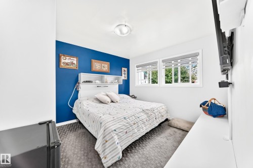 Built-in headboard with integrated shelving, two windows with roller shades, and dark patterned flooring - 10524 128 Avenue Nw, Edmonton, AB - Indoor Photo Showing Bedroom