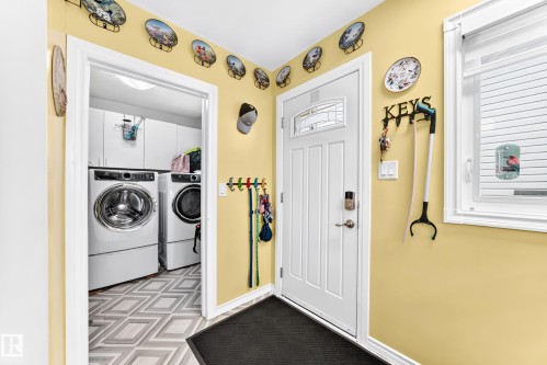 Entry door with decorative glass insert, adjacent window, and laundry area featuring white cabinetry - 10524 128 Avenue Nw, Edmonton, AB - Indoor Photo Showing Laundry Room