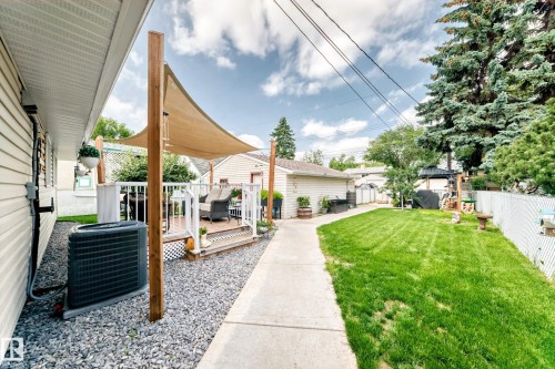 Expansive backyard featuring a manicured lawn, concrete pathway, and a multi-level deck with a shade sail - 10524 128 Avenue Nw, Edmonton, AB - Outdoor