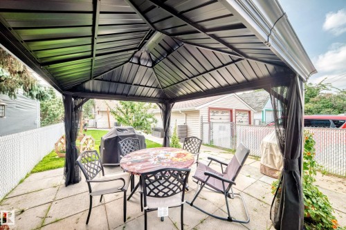 Paved patio area featuring a black metal gazebo with integrated screening, and a chain link fence - 10524 128 Avenue Nw, Edmonton, AB - Outdoor With Deck Patio Veranda With Exterior
