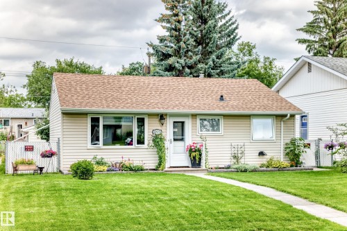Exterior featuring light-colored siding, a brown shingle roof, a front pathway, a manicured lawn, and landscaping with shrubs and perennials - 10524 128 Avenue Nw, Edmonton, AB - Outdoor