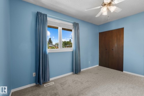 Expansive room featuring light blue walls, gray carpet, a white ceiling fan with integrated lighting, and a window with white trim - 152 Woodstock Nw, Edmonton, AB - Indoor