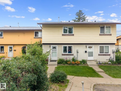 Two-story residential exterior with light-colored siding, concrete walkways, and planted flower beds - 152 Woodstock Nw, Edmonton, AB - Outdoor With Facade