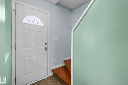 White panel door with an arched decorative glass insert, brass hardware, and wood-finish stair treads - 152 Woodstock Nw, Edmonton, AB - Indoor Photo Showing Other Room