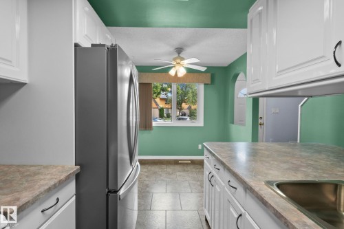 White cabinetry with dark hardware, stainless steel refrigerator, and tiled flooring - 152 Woodstock Nw, Edmonton, AB - Indoor Photo Showing Kitchen