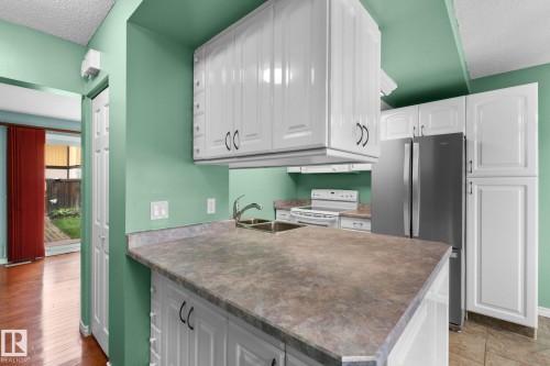 Kitchen featuring white cabinetry, stainless steel refrigerator, double basin sink, and laminate countertops - 152 Woodstock Nw, Edmonton, AB - Indoor Photo Showing Kitchen With Double Sink