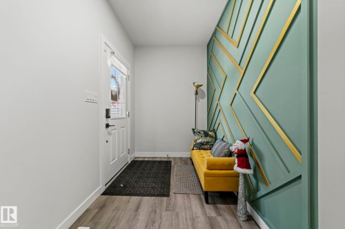 Entryway with wood-finish flooring, white door with upper glass panel, and a decorative accent wall featuring geometric paneling - 16128 31 Avenue Sw, Edmonton, AB - Indoor Photo Showing Other Room