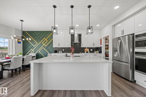Gourmet kitchen with a large central island, stainless steel appliances, white gloss cabinetry, and wood-finish flooring - 16128 31 Avenue Sw, Edmonton, AB - Indoor Photo Showing Kitchen With Upgraded Kitchen
