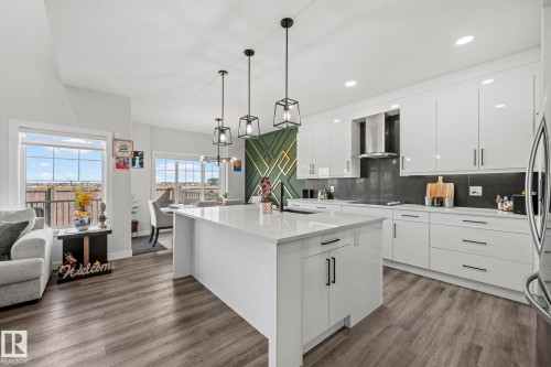 Spacious kitchen with a central island, contemporary pendant lighting, white cabinetry, dark backsplash, and wood-finish flooring - 16128 31 Avenue Sw, Edmonton, AB - Indoor Photo Showing Kitchen With Upgraded Kitchen