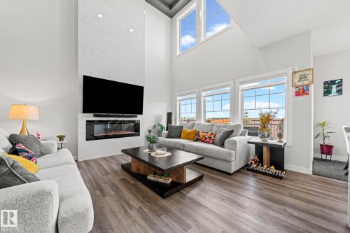 Vaulted ceilings, a full-height stone-finish fireplace, and multiple windows with white trim, featuring wood-finish flooring - 16128 31 Avenue Sw, Edmonton, AB - Indoor Photo Showing Living Room With Fireplace