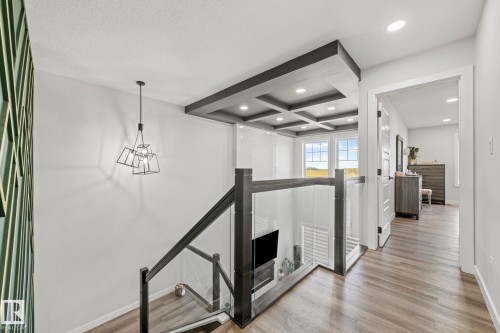 Glass panel railing, coffered ceiling, wood-finish flooring, recessed lighting, and a modern geometric pendant light - 16128 31 Avenue Sw, Edmonton, AB - Indoor Photo Showing Other Room