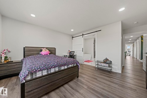 Recessed lighting, wood-finish flooring, white walls, and a sliding barn door - 16128 31 Avenue Sw, Edmonton, AB - Indoor Photo Showing Bedroom