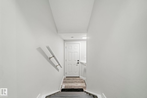 White interior door with black hardware, wood-finish flooring, and a wall-mounted handrail - 16128 31 Avenue Sw, Edmonton, AB - Indoor Photo Showing Other Room