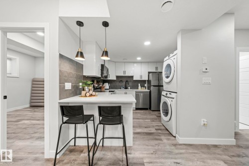Contemporary kitchen with white cabinetry, light countertops, integrated stainless steel appliances, and wood-finish flooring - 16128 31 Avenue Sw, Edmonton, AB - Indoor