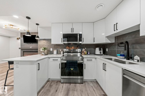 White cabinetry with black hardware, stainless steel appliances, light wood-finish flooring, white countertops, and a dark tile backsplash - 16128 31 Avenue Sw, Edmonton, AB - Indoor Photo Showing Kitchen With Double Sink With Upgraded Kitchen