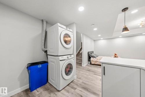 Stackable washer and dryer appliances, wood-finish flooring, recessed lighting, and a contemporary pendant light fixture - 16128 31 Avenue Sw, Edmonton, AB - Indoor Photo Showing Laundry Room