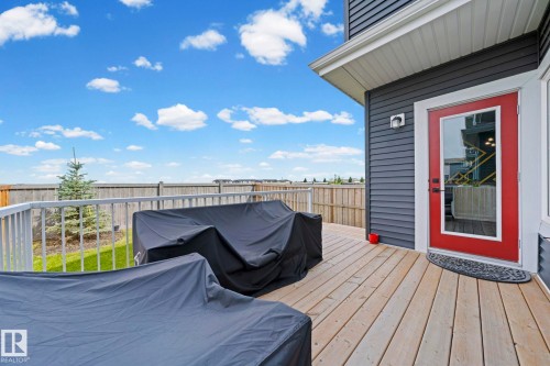 Expansive wood-finish deck with white railings, a red glass-panel door, and dark gray siding - 16128 31 Avenue Sw, Edmonton, AB - Outdoor With Deck Patio Veranda With Exterior
