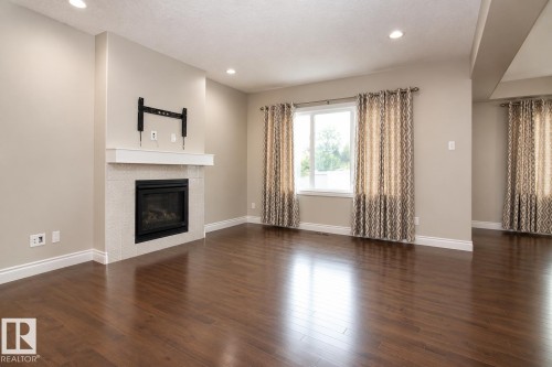 Hardwood-finish flooring, recessed lighting, gas fireplace with tile surround, white mantel, and large window - 7274 Morgan Road Nw, Edmonton, AB - Indoor Photo Showing Living Room With Fireplace