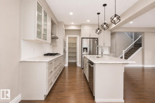 Kitchen featuring a central island with a sink, stainless steel appliances, light cabinetry, a white subway tile backsplash, and wood-finish flooring - 7274 Morgan Road Nw, Edmonton, AB - Indoor Photo Showing Kitchen With Upgraded Kitchen