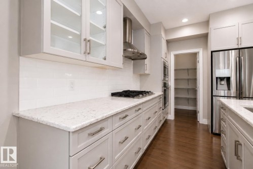 Kitchen featuring white shaker-style cabinetry, stainless steel appliances, a gas cooktop with an exhaust hood, and a walk-in pantry - 7274 Morgan Road Nw, Edmonton, AB - Indoor Photo Showing Kitchen With Upgraded Kitchen