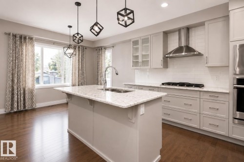 Kitchen featuring a central island with a double basin sink, stainless steel appliances, light gray cabinetry, wood-finish flooring, and pendant lighting - 7274 Morgan Road Nw, Edmonton, AB - Indoor Photo Showing Kitchen With Double Sink With Upgraded Kitchen