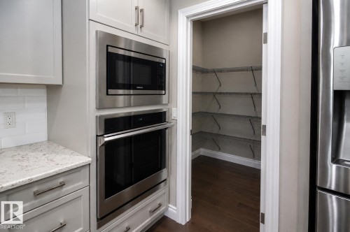 Built-in stainless steel microwave and oven, light-toned cabinetry, white subway tile backsplash, and a walk-in pantry with wire shelving - 7274 Morgan Road Nw, Edmonton, AB - Indoor Photo Showing Kitchen