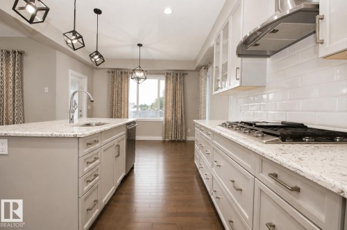 Kitchen featuring an island with an undermount sink, light-toned countertops, white shaker cabinetry, and wood-finish flooring - 7274 Morgan Road Nw, Edmonton, AB - Indoor Photo Showing Kitchen With Upgraded Kitchen