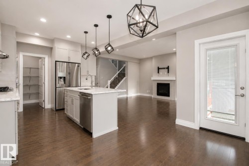 Hardwood-style flooring throughout, kitchen island with integrated sink, stainless steel appliances, built-in fireplace with mantel, and a dedicated pantry - 7274 Morgan Road Nw, Edmonton, AB - Indoor Photo Showing Kitchen