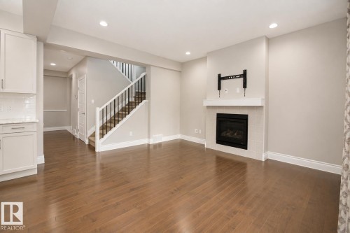 Hardwood flooring throughout, a gas fireplace with a tiled surround and white mantel, recessed lighting, and a staircase with dark wood treads and white risers - 7274 Morgan Road Nw, Edmonton, AB - Indoor With Fireplace