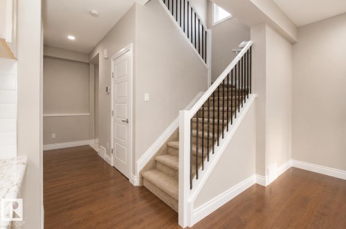Wood-finish flooring throughout, carpeted staircase with wrought iron balusters, white trim, recessed lighting, and a paneled interior door - 7274 Morgan Road Nw, Edmonton, AB - Indoor Photo Showing Other Room